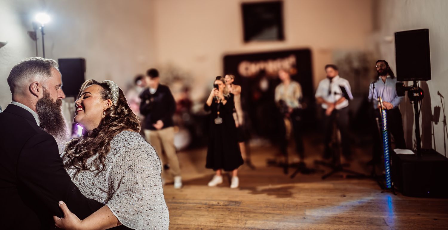 A couple shares a romantic dance moment on a rustic wooden floor at an indoor reception venue.