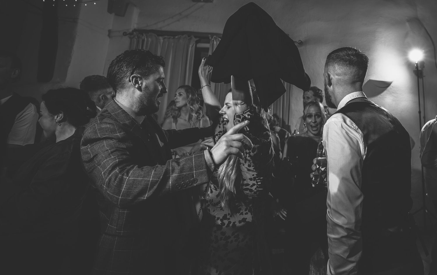Wedding guests dance and celebrate on a dimly lit dance floor during an evening reception party.