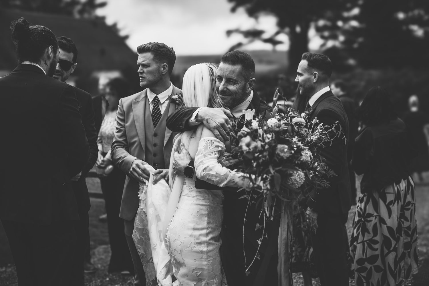 A black and white photo shows people celebrating at what appears to be a wedding reception outdoors.