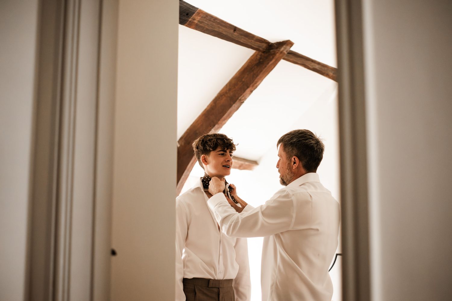 Intimate moments captured during wedding preparations in a sunlit room with wooden beams.