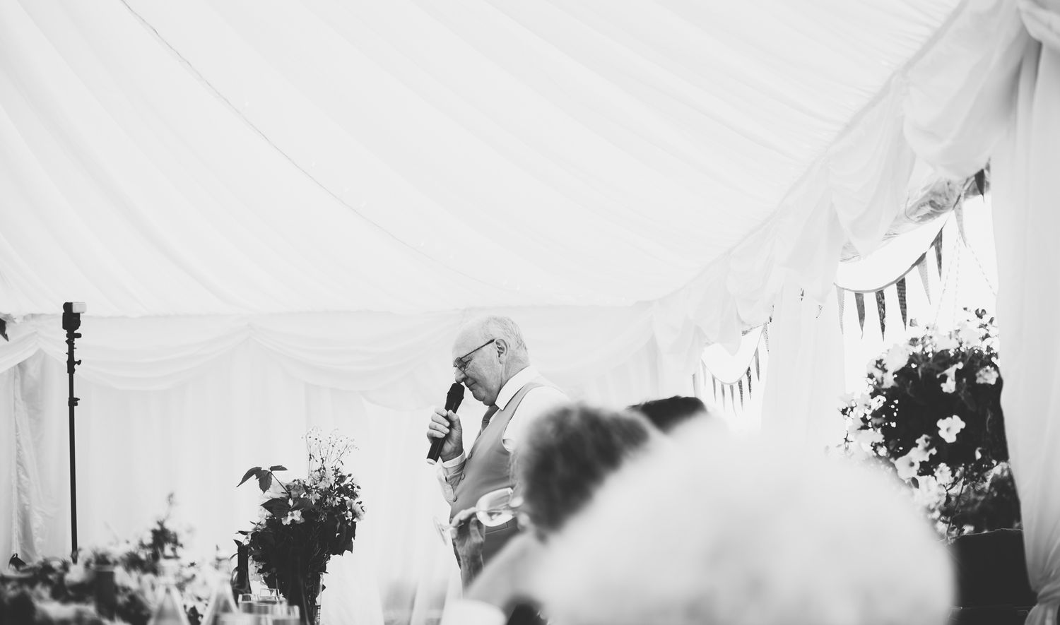 A black and white wedding ceremony photo shows guests seated in rows with white floral arrangements along the aisle.