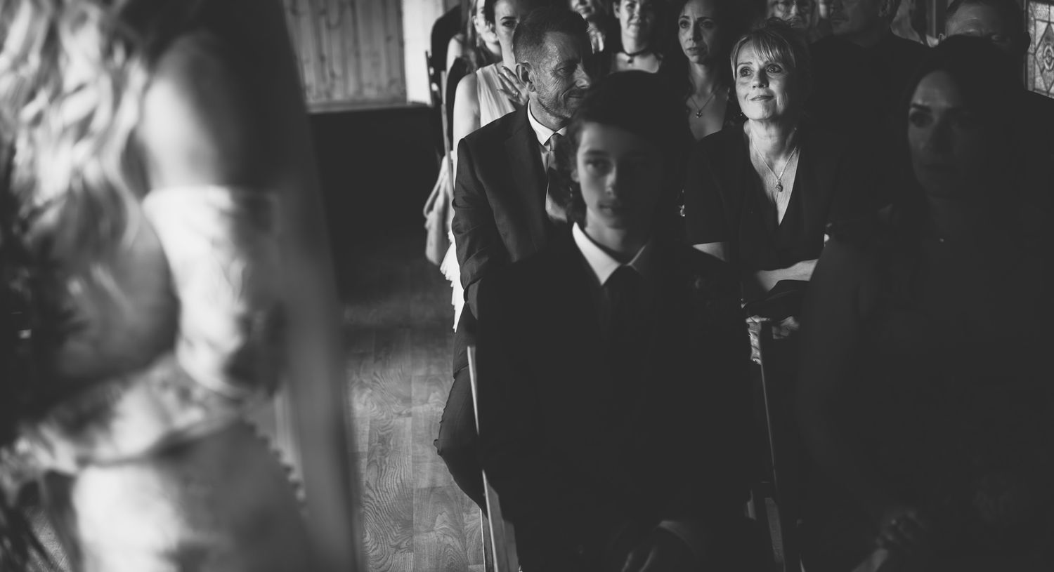 A black and white film still shows people gathered in a dimly lit interior space.