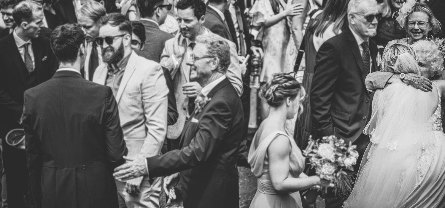 Black and white photo of a crowded wedding reception with people dancing and mingling in formal attire.