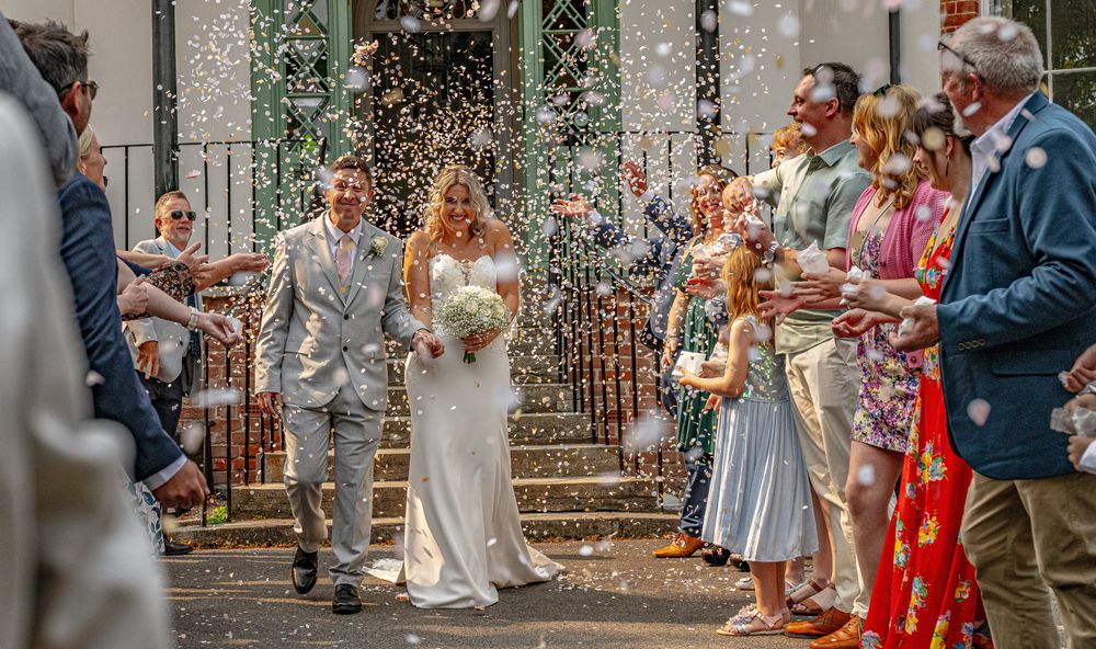 Wedding guests throw confetti over the newlyweds during an outdoor celebration at a rustic venue.
