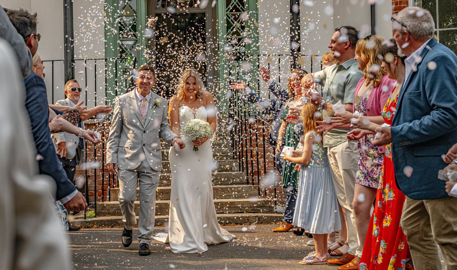 Wedding guests throw confetti over the newlyweds during an outdoor celebration at a rustic venue.