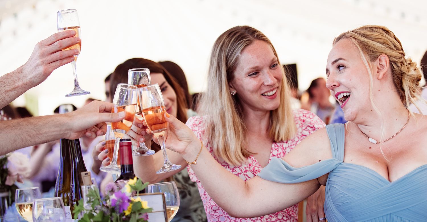 Wedding guests raise champagne glasses in celebration during an outdoor reception toast.