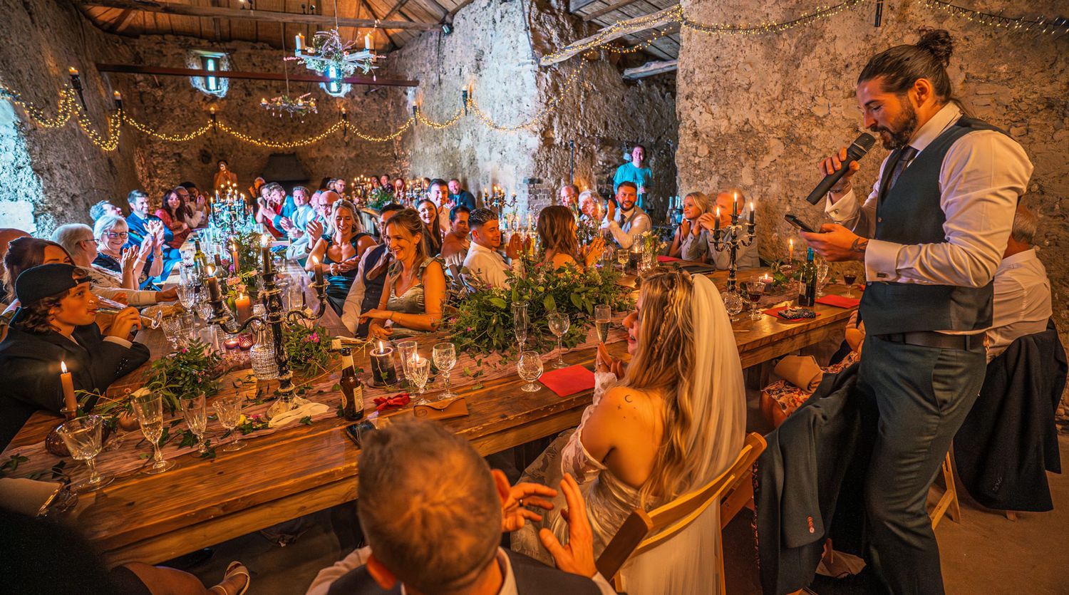 Large crowd of people enjoying a festive evening celebration in a rustic wooden venue with string lights overhead.