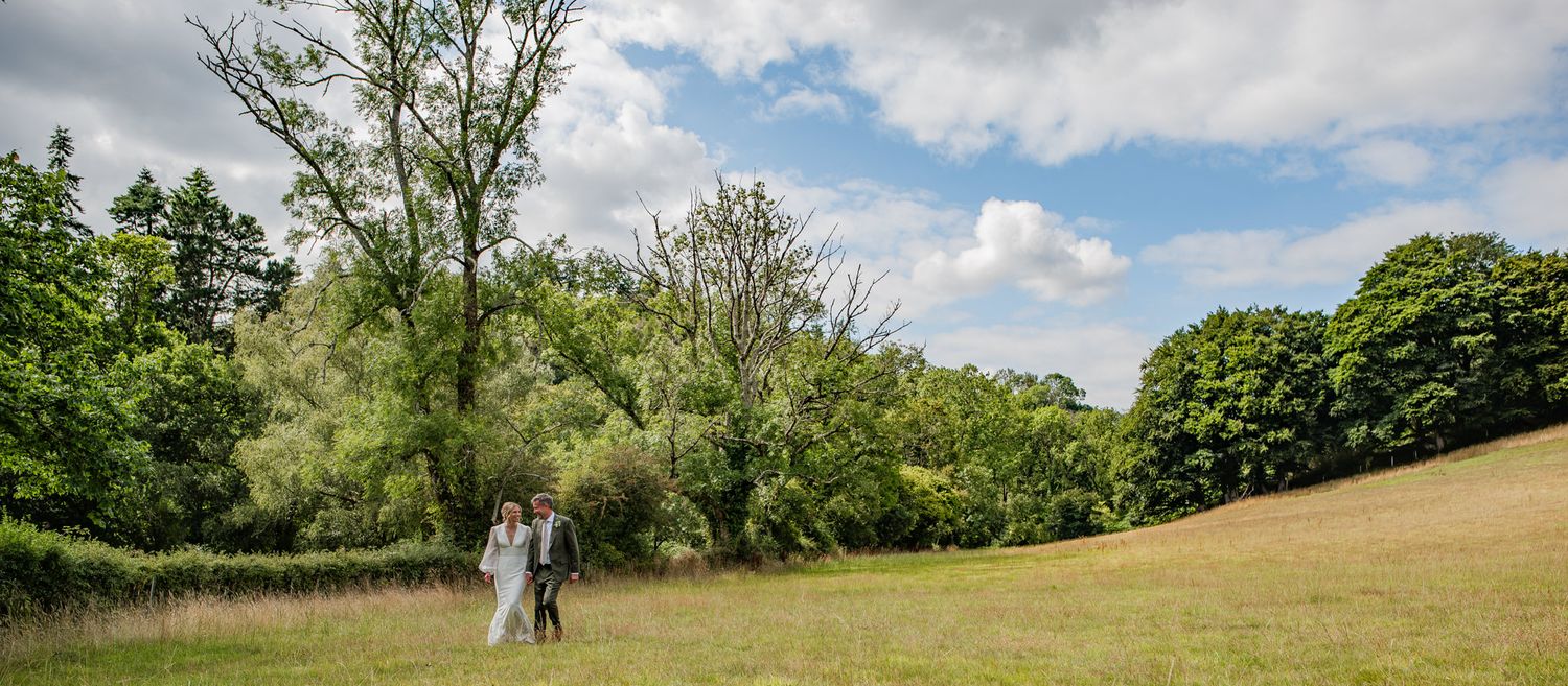A panoramic view of rolling green hills with scattered trees and white clouds in a bright summer sky.