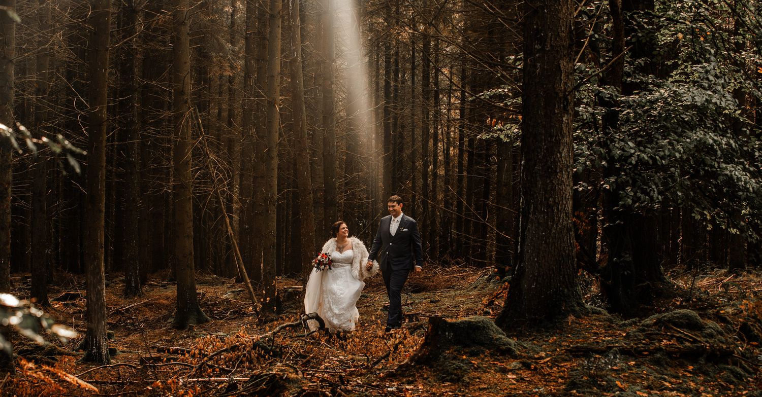 A moody forest wedding scene with tall evergreen trees and warm autumn lighting creating a romantic atmosphere.