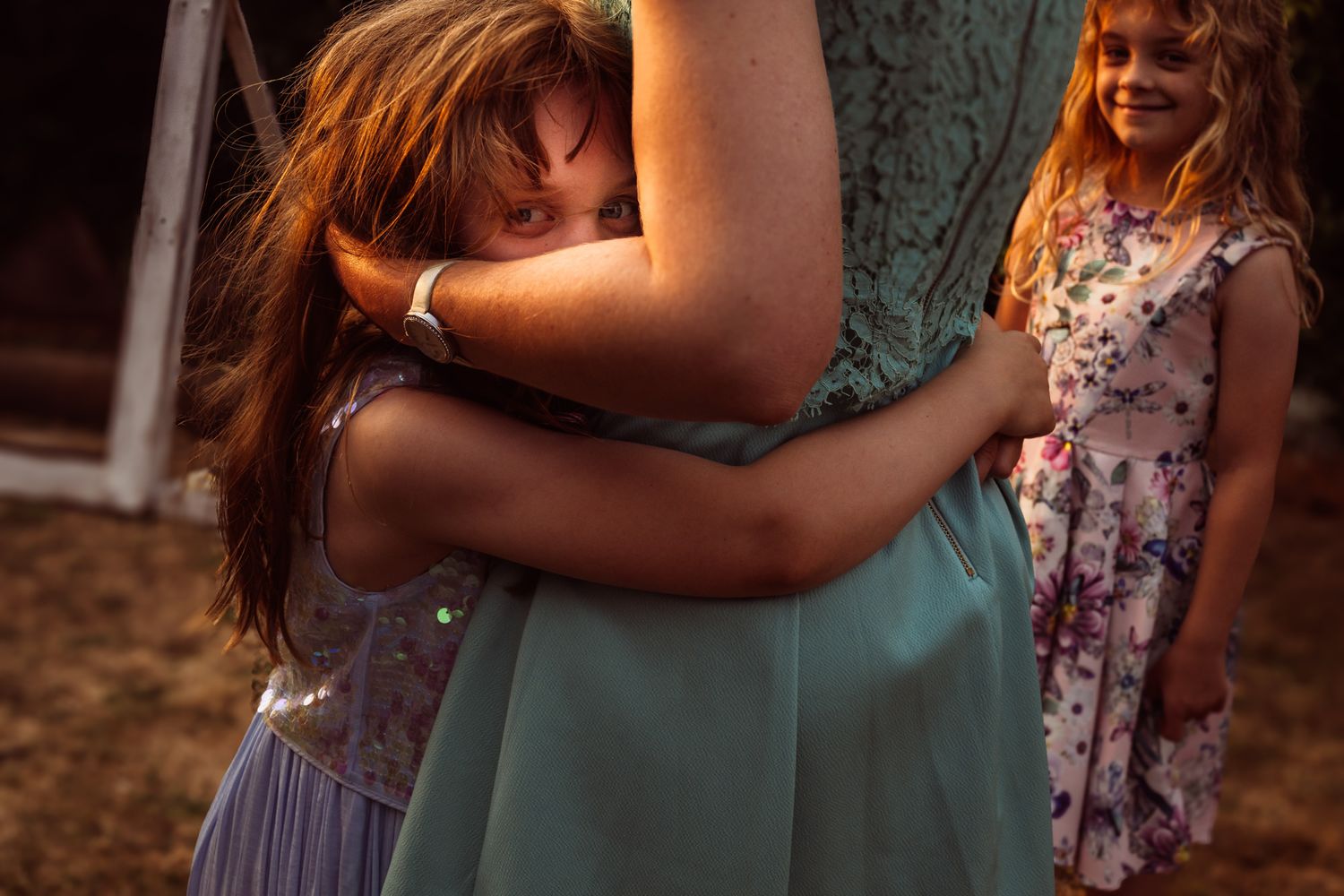 A couple in floral and green attire embrace during a romantic golden hour photoshoot in a rustic outdoor setting.