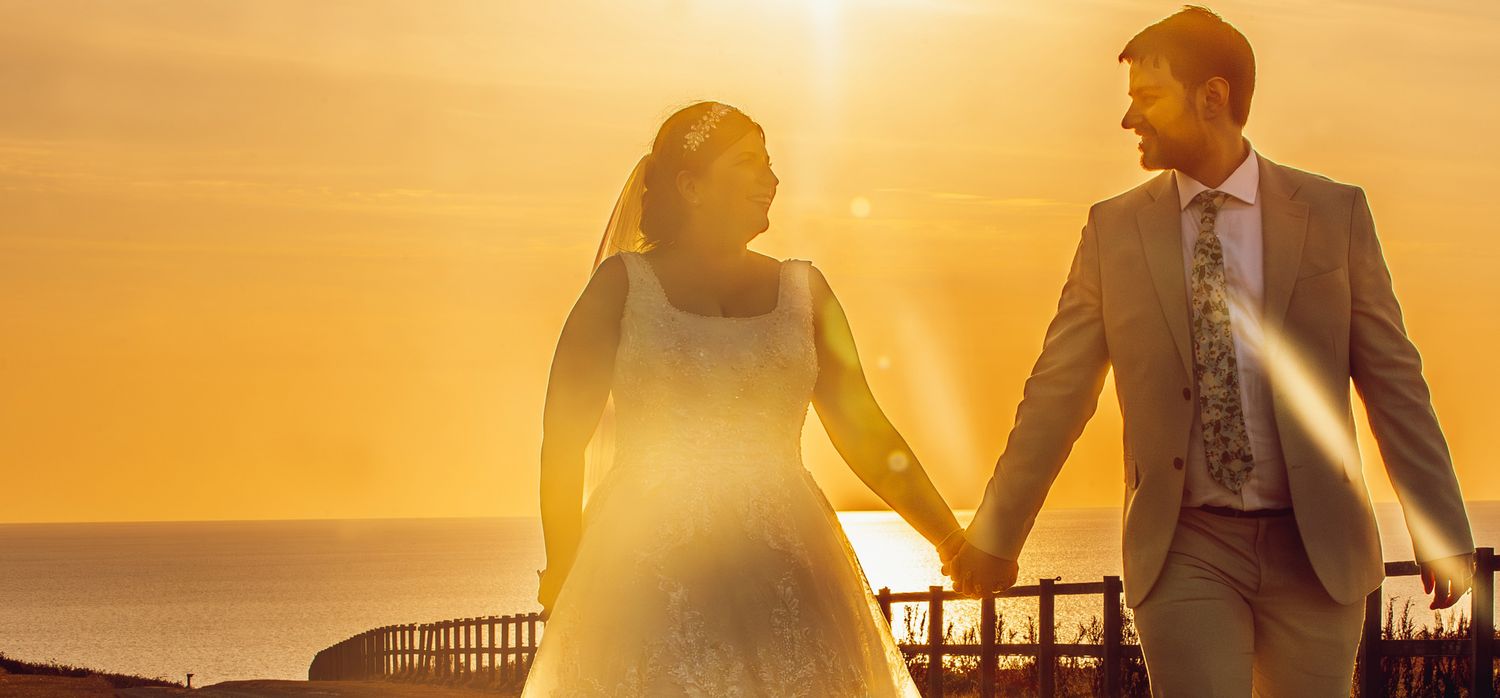 Silhouetted figures stand against a warm golden sunset sky with architectural elements in view.