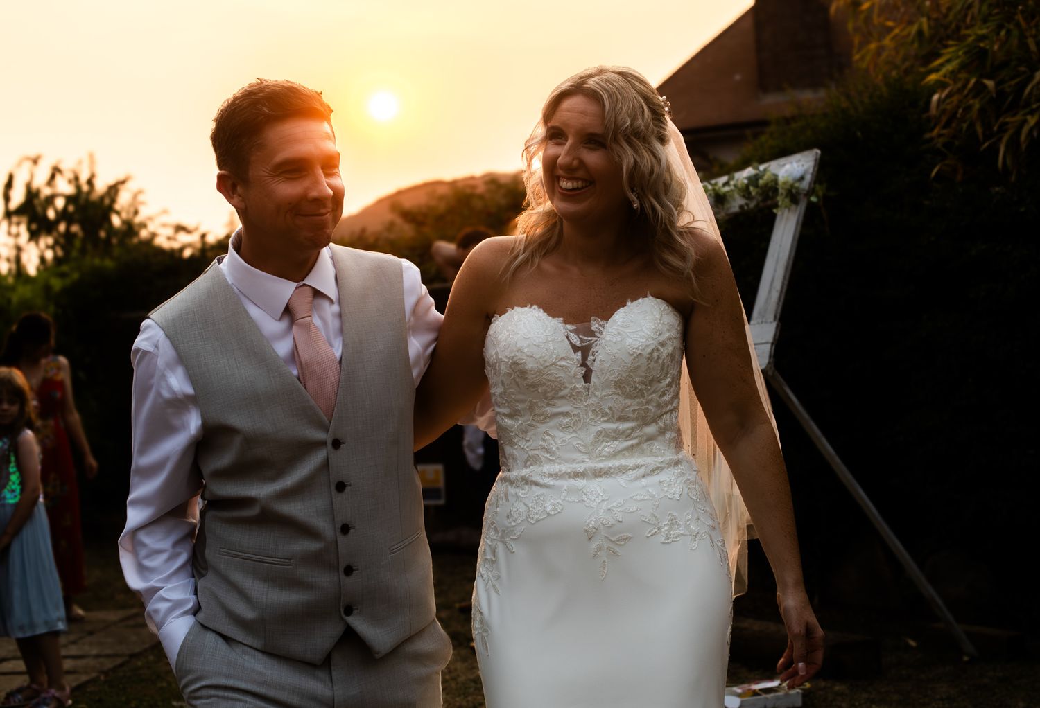 A couple in wedding attire dance together during sunset at an outdoor reception.