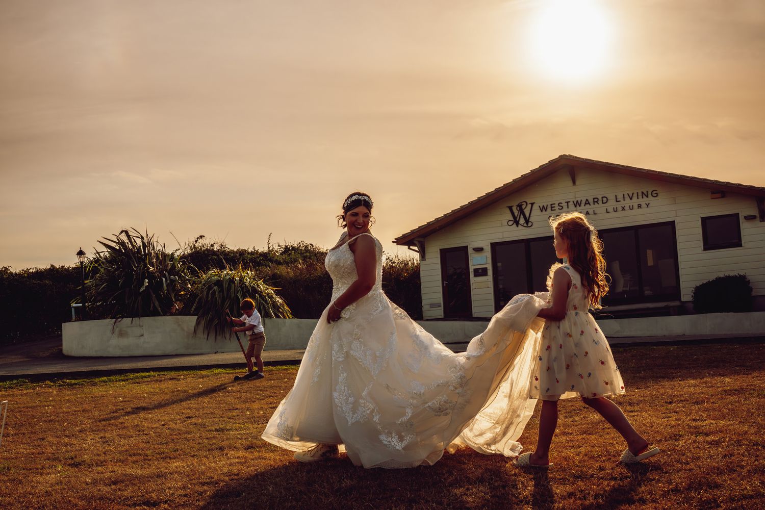 A sunset wedding scene with people in flowing white dresses playing and twirling on a rustic dirt field.