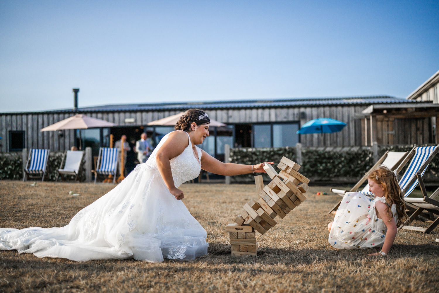 A bride in a white wedding dress lies on the beach while waves crash nearby, creating a romantic seaside moment.