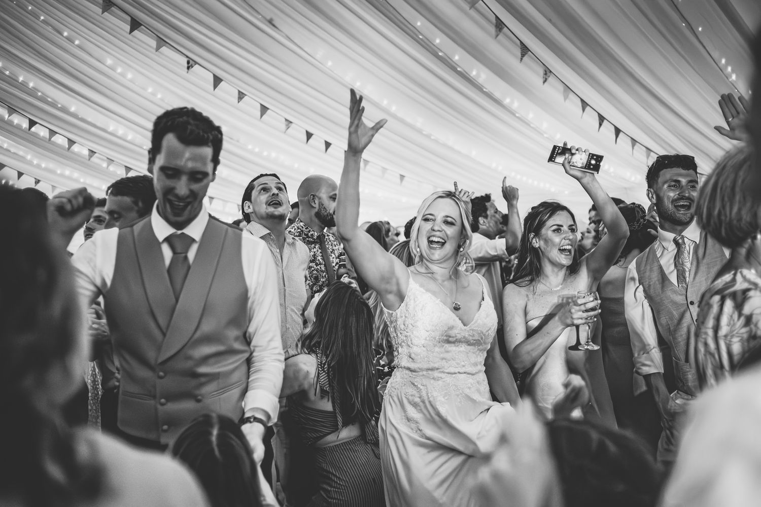 Wedding guests dance and celebrate together on a lively dance floor at an indoor reception venue.
