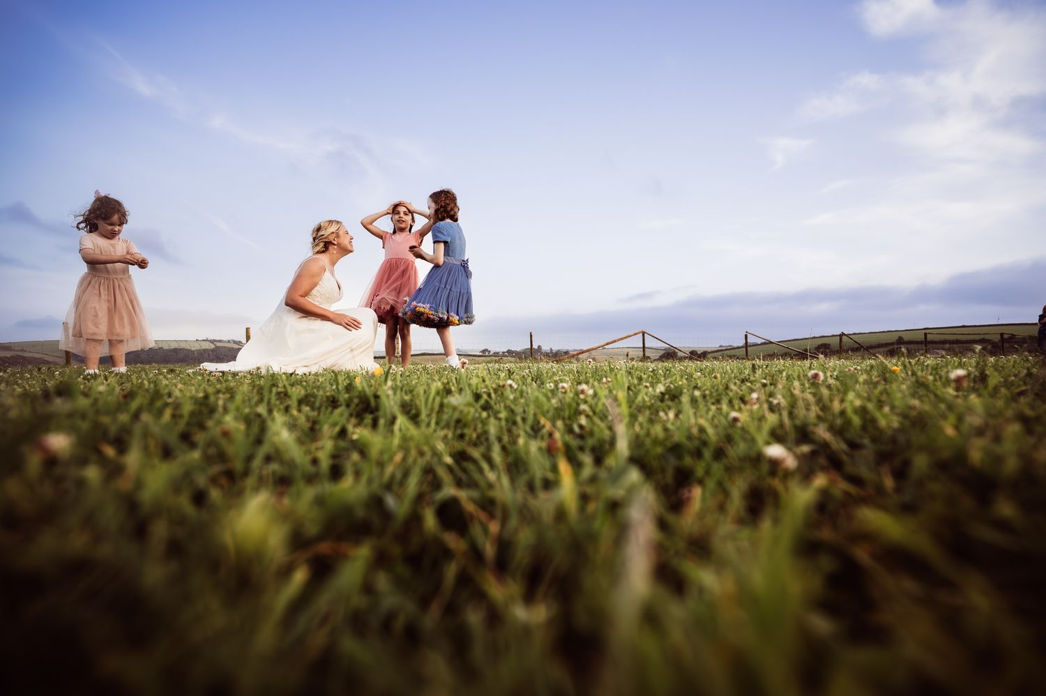 A couple walks hand in hand through a lush green vineyard with mountains in the distance on a sunny day.