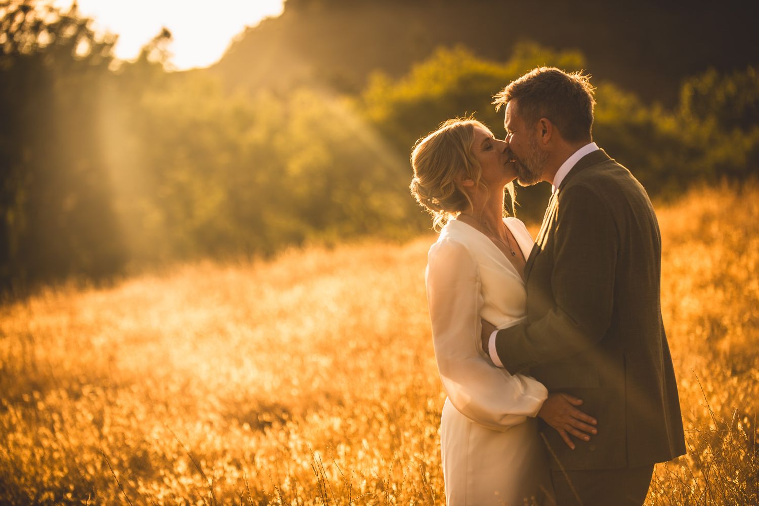 Romantic couple embraces in golden sunlit field during sunset creating silhouettes against warm autumn light.