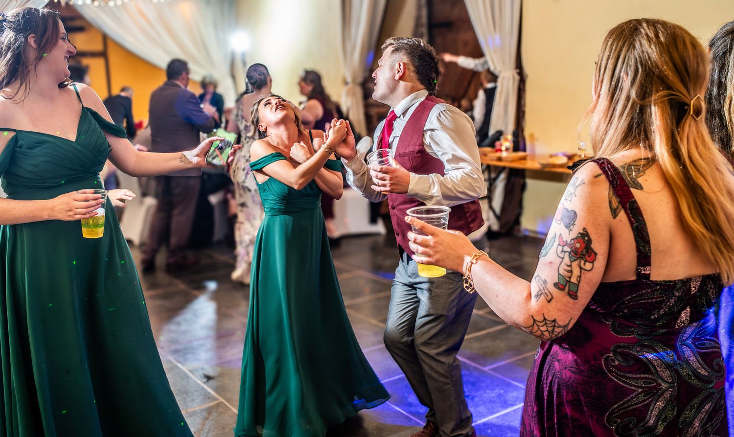 People dancing together in pairs during a social dance event with colorful lighting and casual atmosphere.