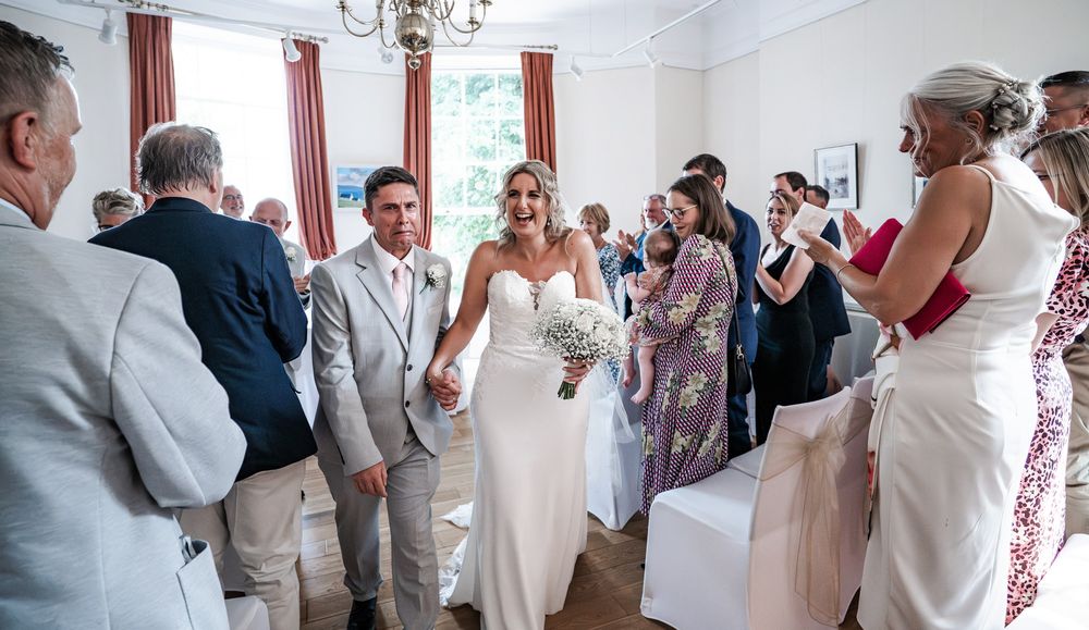 Wedding guests gather in a bright indoor venue with white walls and red curtains during a celebration.