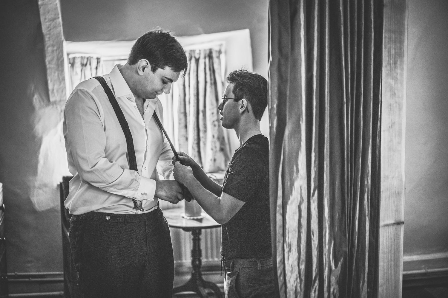 Black and white photo showing preparations in a room with curtains and formal attire.