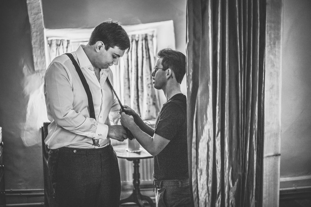 Black and white photo showing preparations in a room with curtains and formal attire.