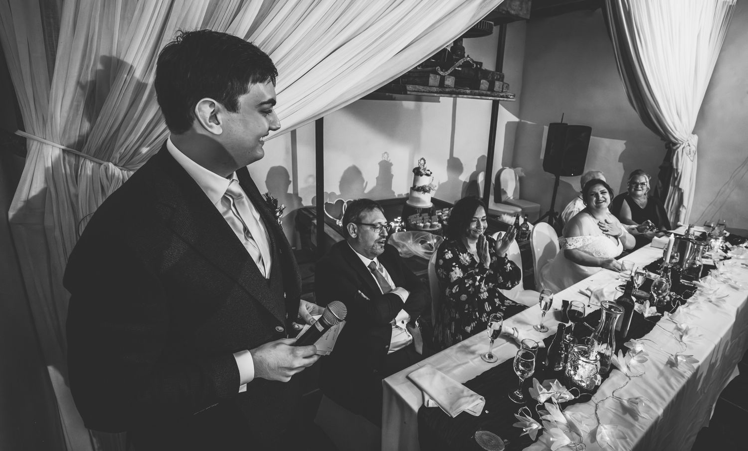 Wedding guests enjoy a lively reception celebration in a white tent decorated with elegant draping and lighting.