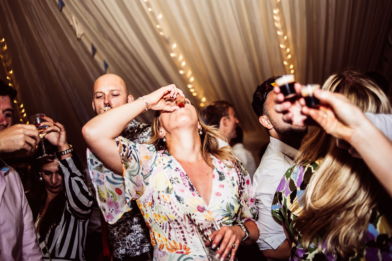 Wedding party guests dancing and celebrating on a lively dance floor with festive lighting in the background.