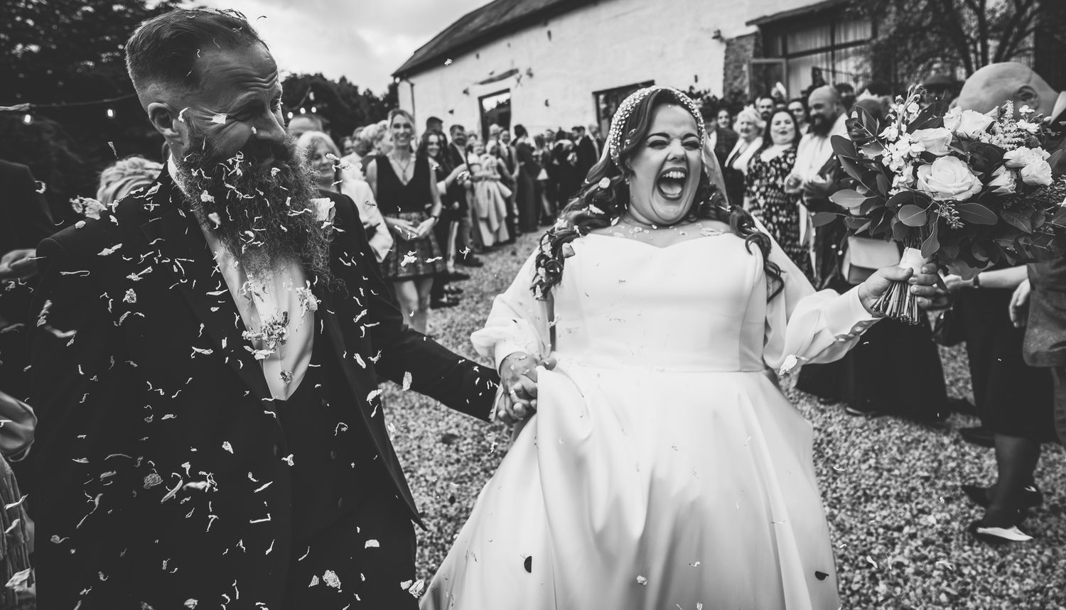 Wedding guests celebrate by throwing confetti and cheering at an outdoor celebration.
