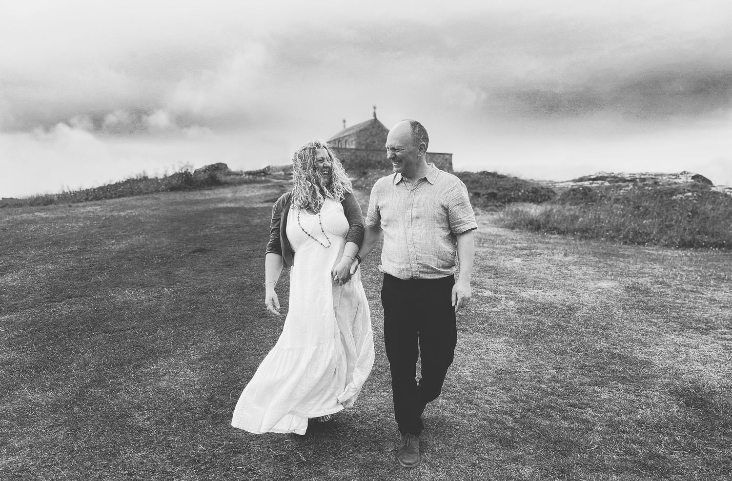 A couple walks hand in hand along a scenic hilltop path in black and white photography.