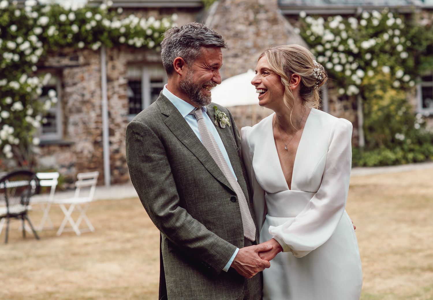 A couple shares a joyful moment together in formal attire on a sunny day outside a stone building.