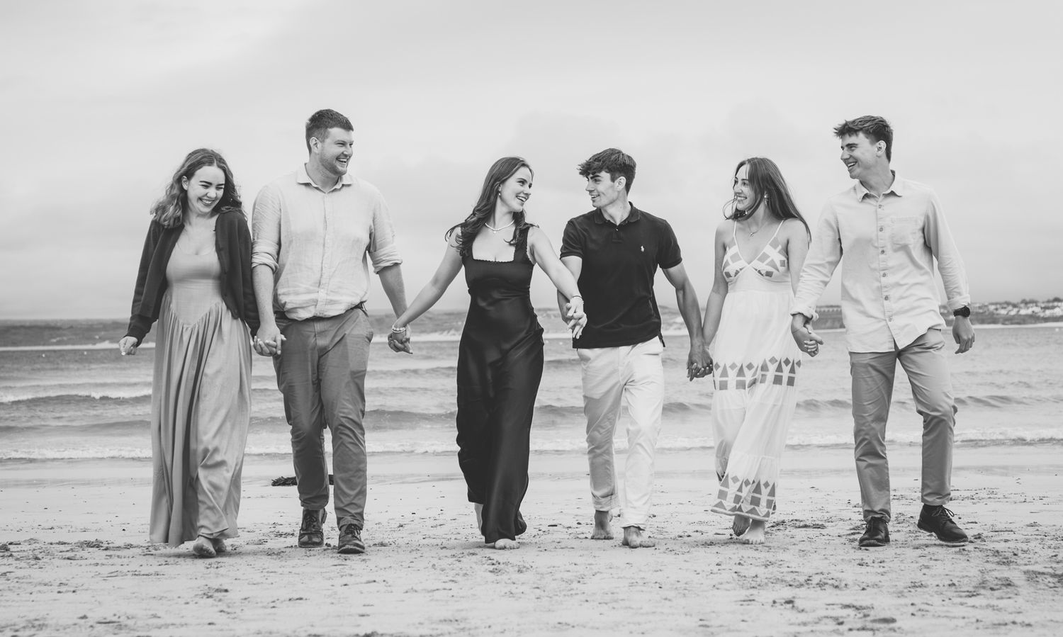 A series of black and white beach photos showing people walking together along the shoreline at sunset.