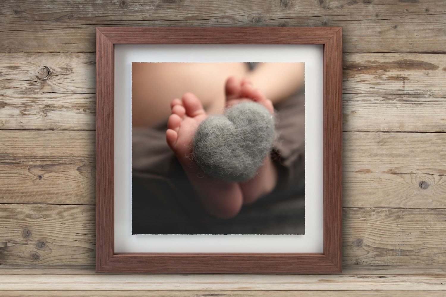 A series of framed photographs showing close-up details of baby feet and hands arranged on a rustic wooden wall.