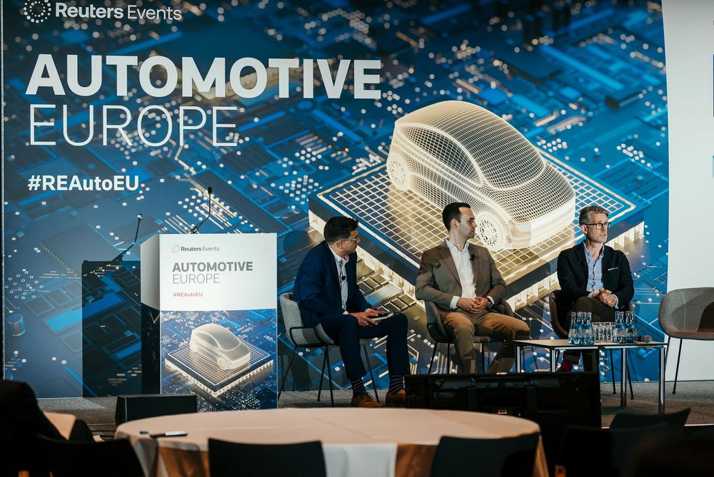 Business conference stage setup with Automotive Europe branding and blue circuit board graphics in the background.