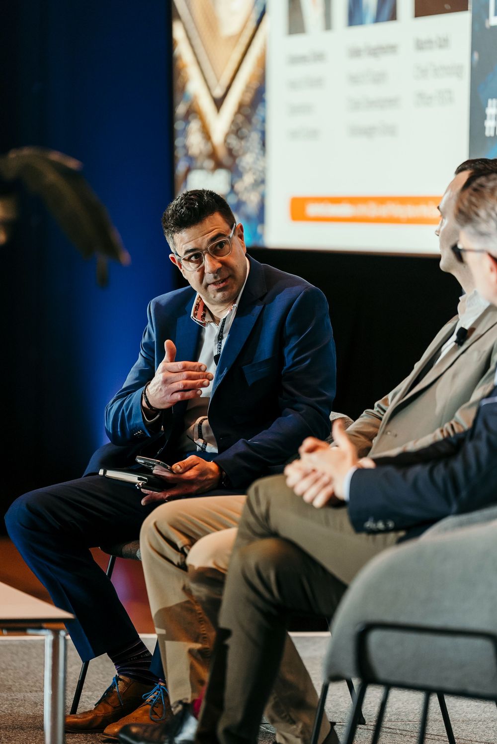 Business professionals in dark suits engage in animated discussion while seated during a professional conference.