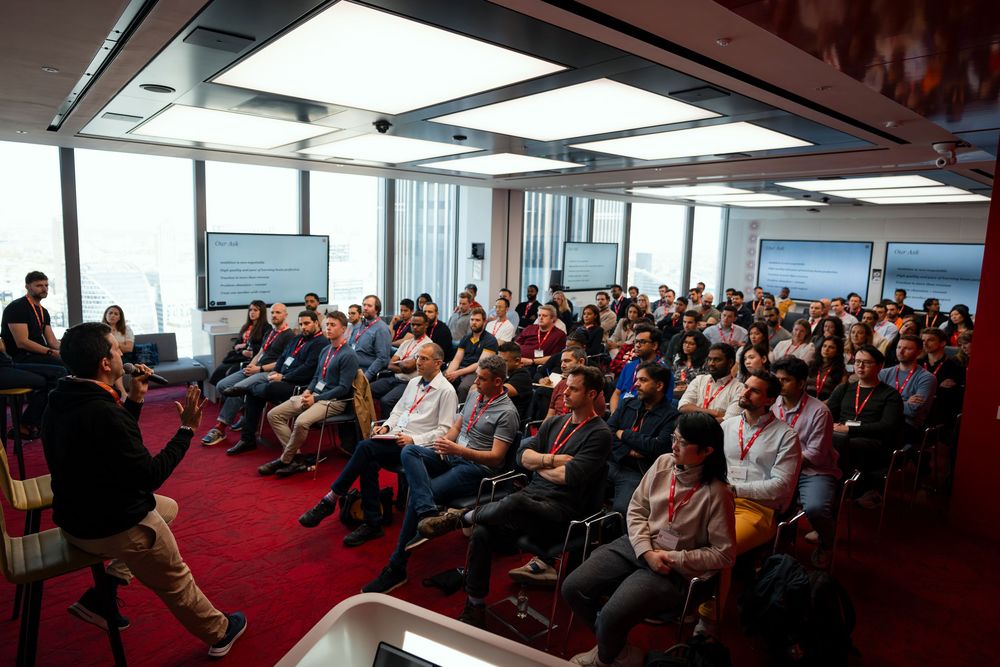 Business professionals gathered in a modern conference room with red carpeting for a corporate presentation or meeting.