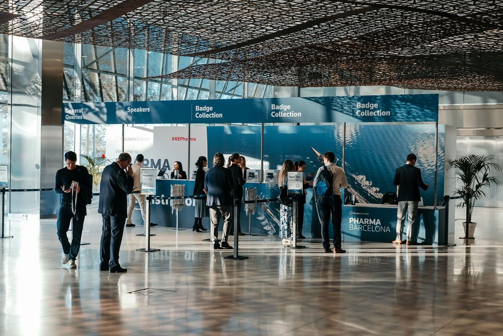 People gather in a modern corporate lobby with glass walls and blue wall displays during a business event.