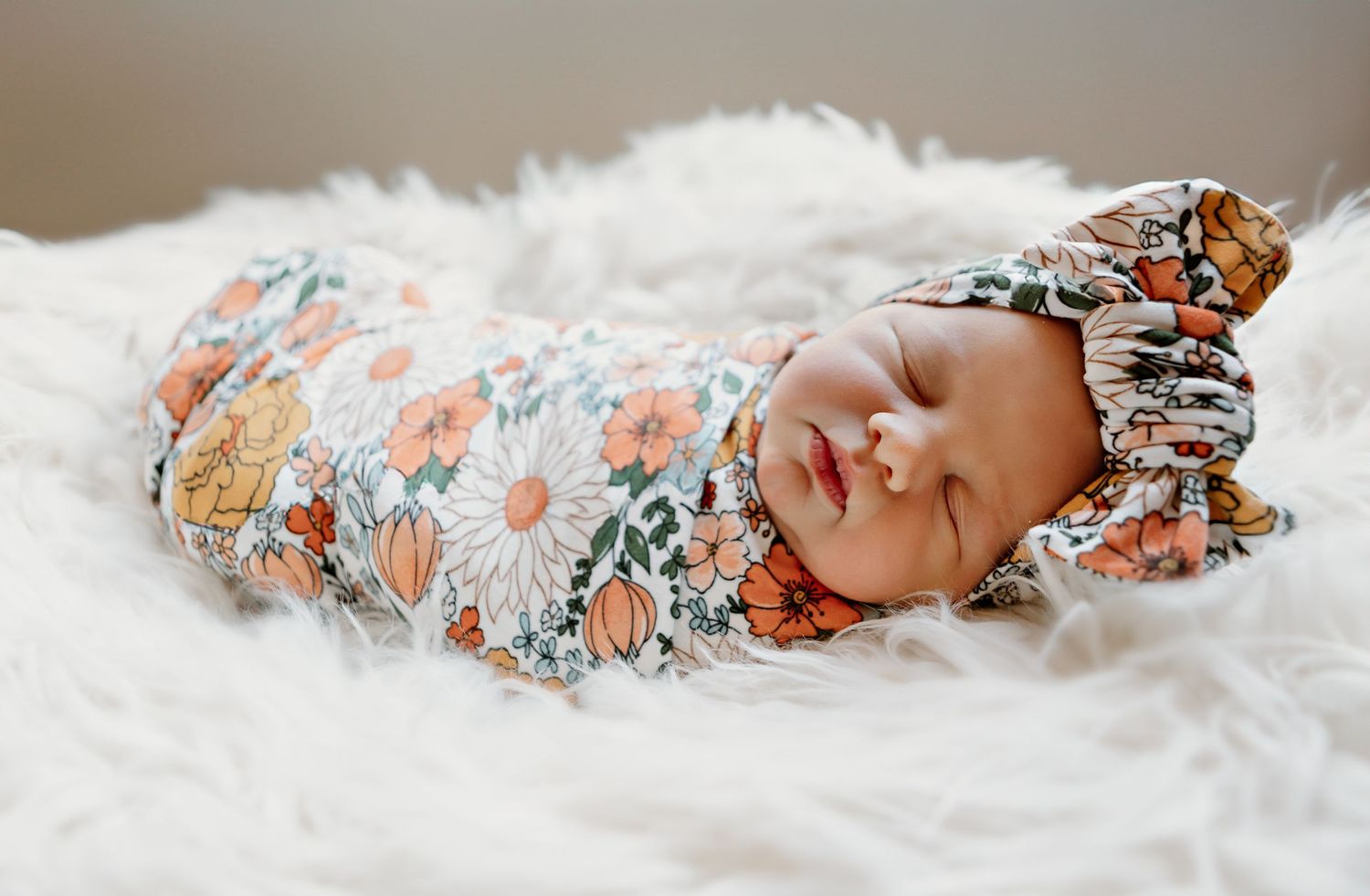 Sleeping newborn baby wrapped in floral swaddle on white fluffy blanket.