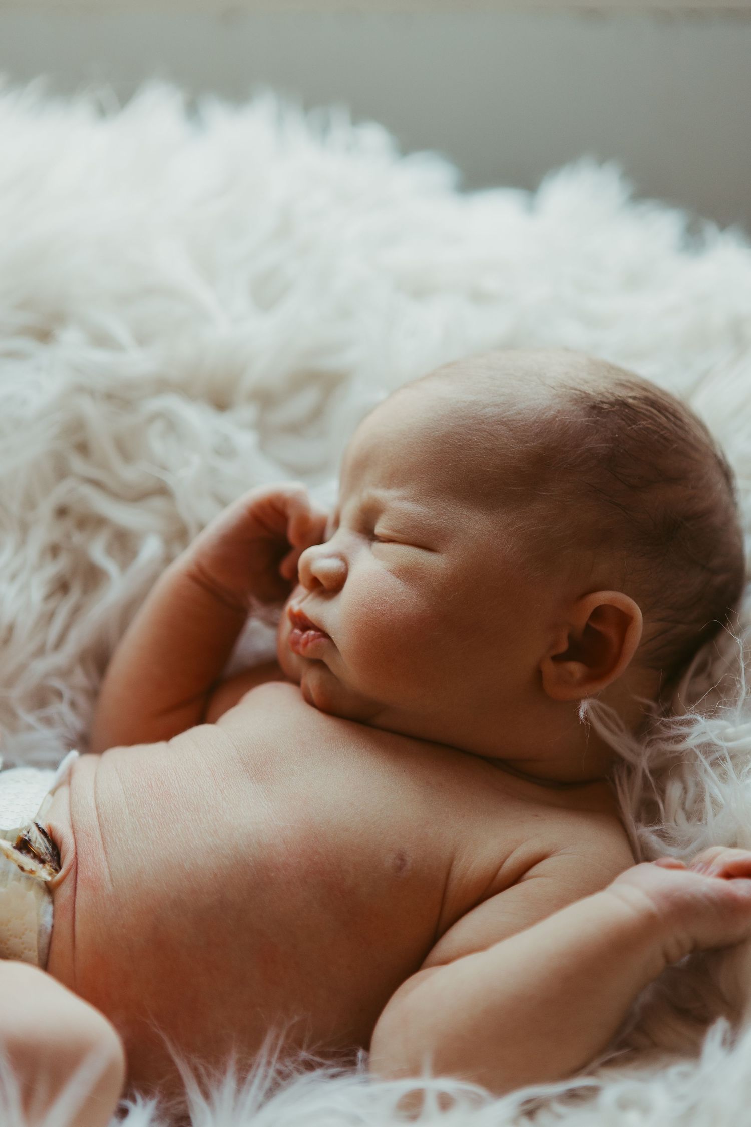 Sleeping newborn baby lying on soft white fur background.