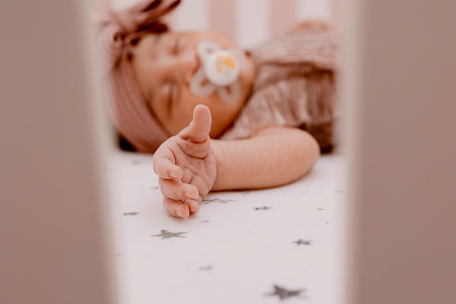 Baby resting on soft pink background with gentle lighting.
