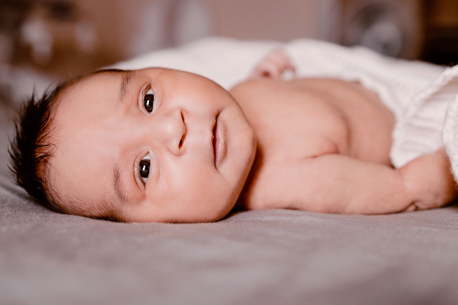 Baby lying on soft blanket in natural light setting.