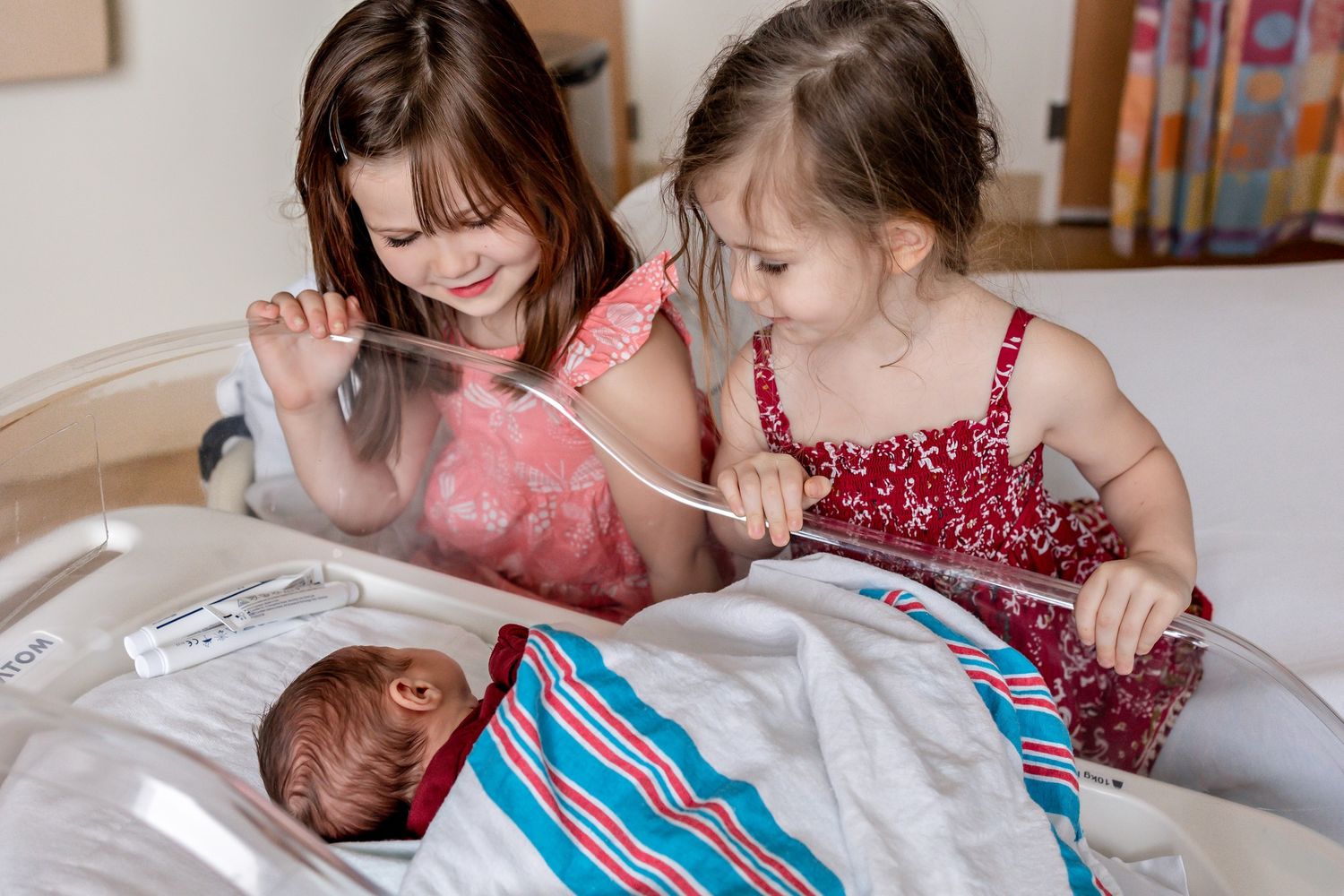 Children gathered around a baby on white bedding with a teddy bear nearby.