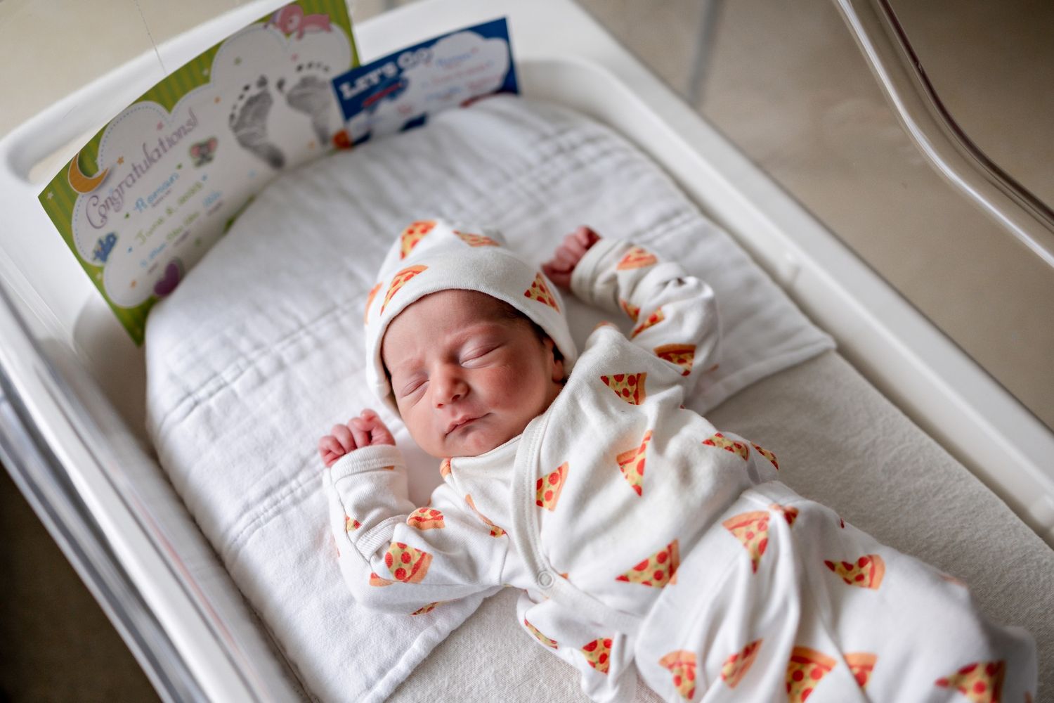 Baby wearing white onesie with orange pattern resting on light colored bedding.