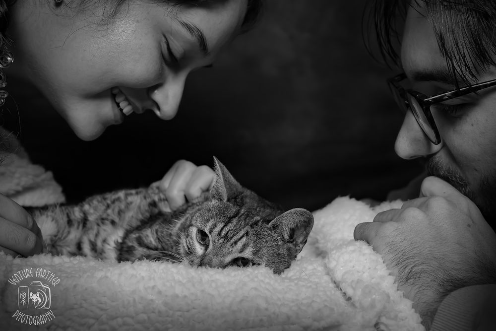 A cat lies contentedly between two people in a tender black and white photograph.