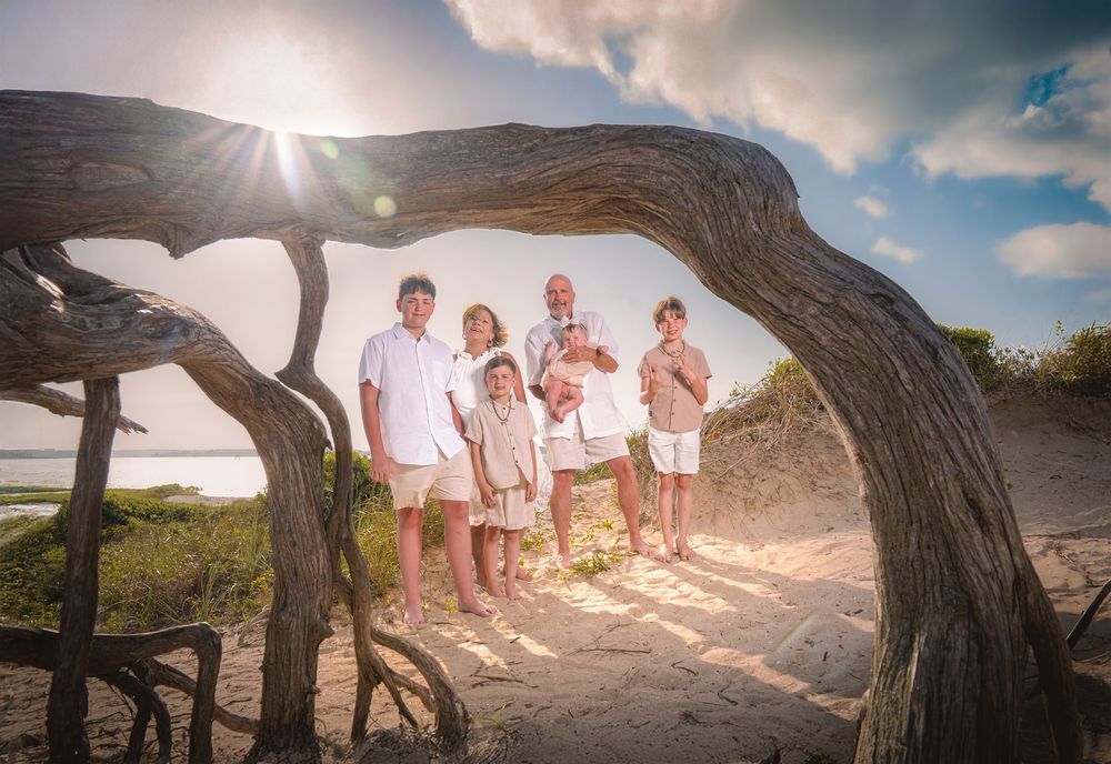 Group of people walking along a scenic beach path framed by natural wooden archways during sunset.