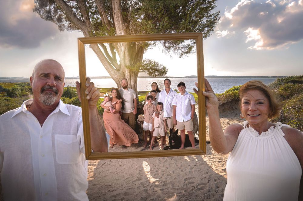 A group of people gather for a sunset beach wedding ceremony under a wooden arbor on a sandy shore.