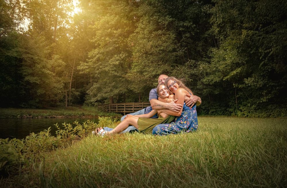 A romantic couple lies in a sunlit meadow during golden hour as sunbeams filter through surrounding trees.