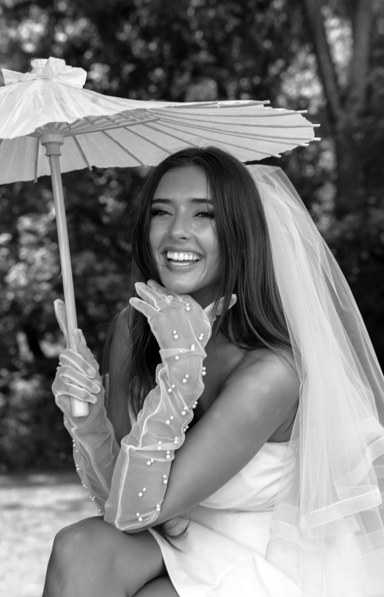 A series of black and white bridal portraits featuring a white parasol and flowing veil in an outdoor garden setting.