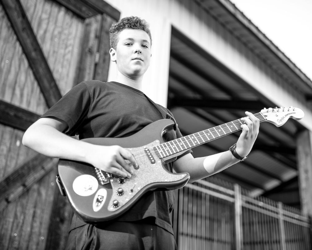 A teenager poses with his guitar against a rustic wooden background in Colleyville, Texas