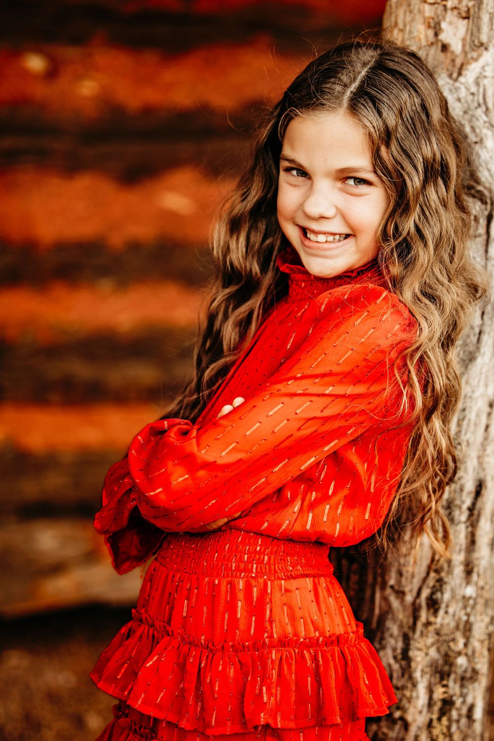A girl in a bright red ruffled dress poses against a rustic wooden wall with warm autumn lighting in Colleyville, TX