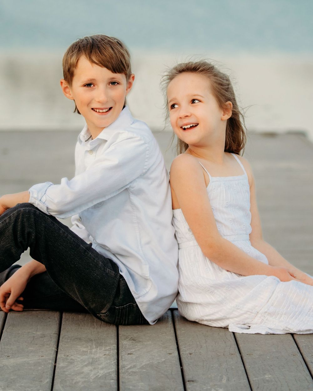 Two children in white outfits sit on a wooden deck while laughing and playing together in Fort Worth
